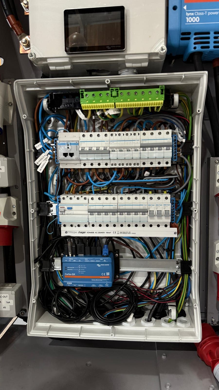 Interior de um quadro elétrico aberto, com duas filas de disjuntores e diferenciais em calha, barramentos de terra e de neutro no topo e um controlador Victron Cerbo GX montado por baixo.